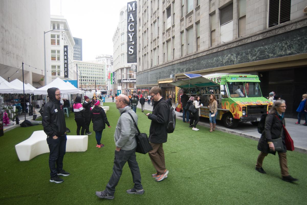 Pedestrians and shoppers on artificial grass at 2018 Winter Walk event near Macy's on Stockton Street, with food truck and market tents visible.