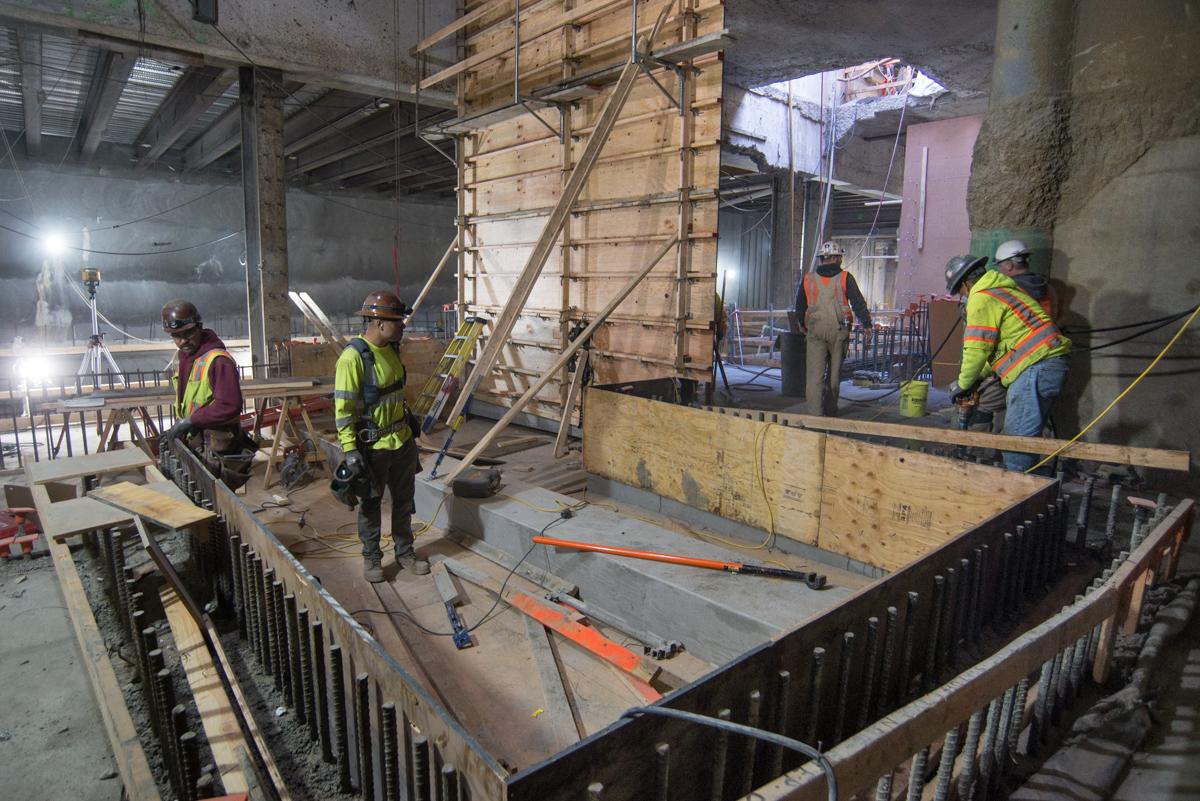 Construction workers in safety vests build concrete forms for underground transit station floor slab and walls.