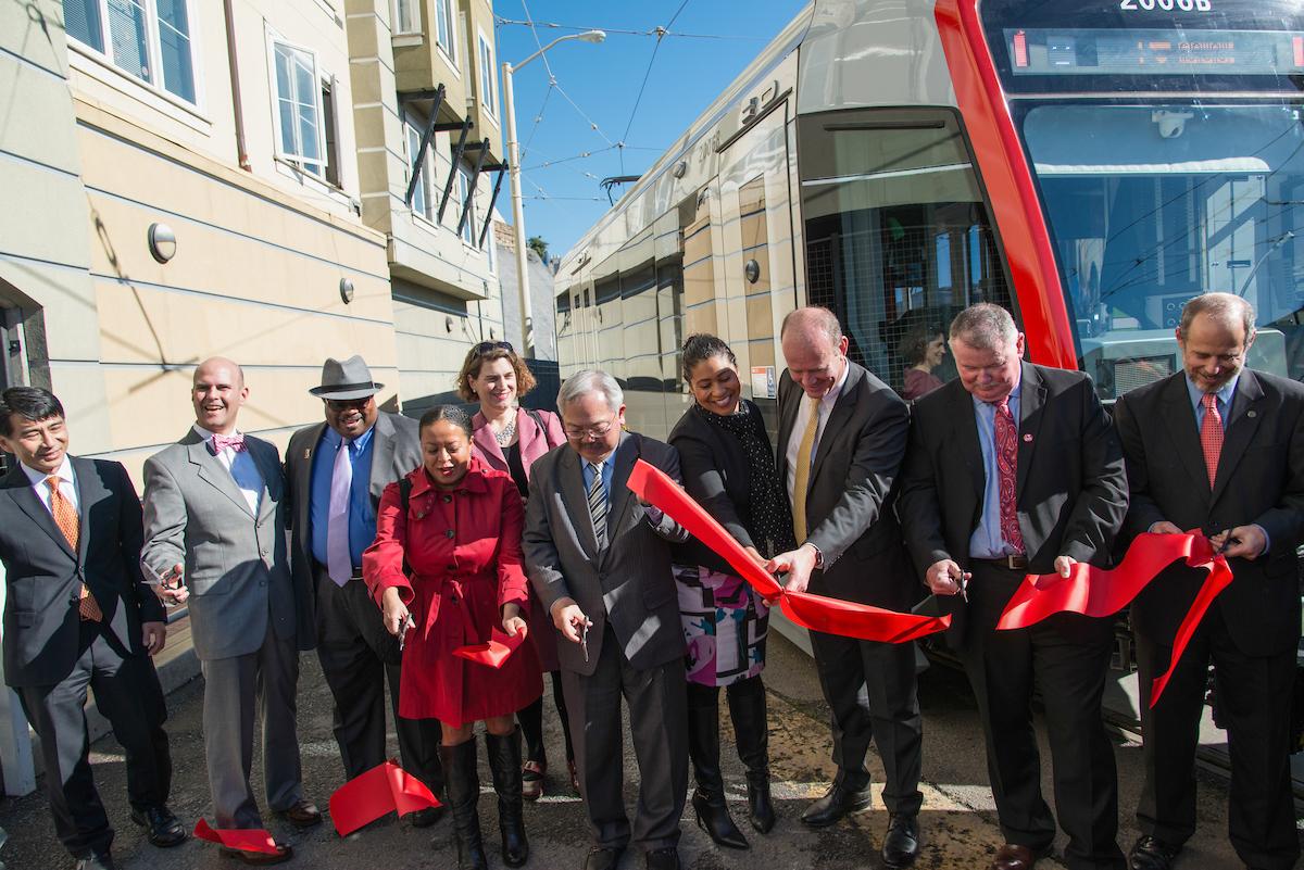Group of officials and community leaders cutting red ribbon at new light rail vehicle ceremony
