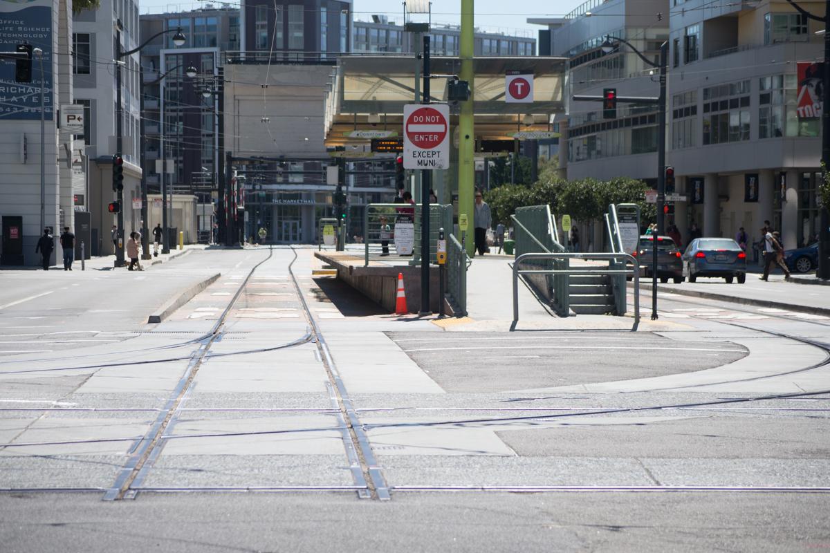 Light rail tracks and street infrastructure under construction on urban street with buildings and pedestrians visible.