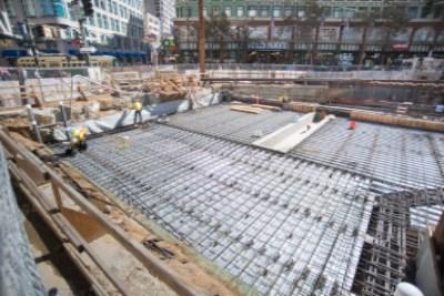 Construction site with rebar grid laid over steel panels at Union Square Garage, downtown buildings visible above.