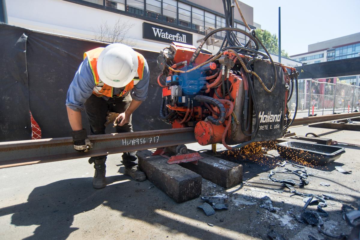 Worker inspecting rail welding equipment on truck bed at transit maintenance facility.