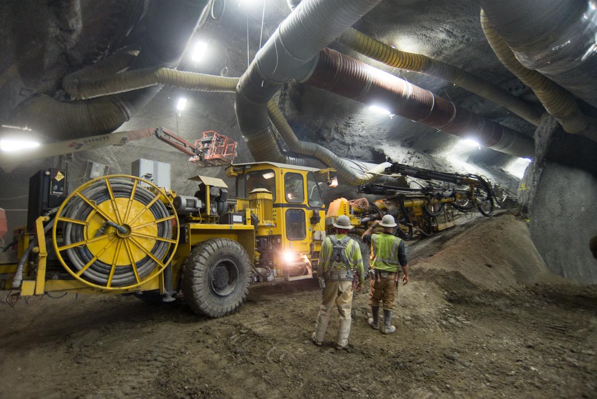 Workers in hard hats operate heavy machinery inside an underground tunnel during construction work.