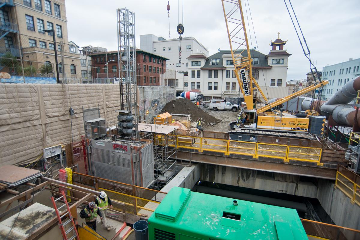 Construction site with yellow crane, excavation equipment, and concrete shaft structure in urban setting.