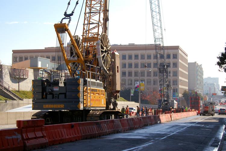 Large construction crane and equipment on 4th Street with red barriers and urban buildings in background.