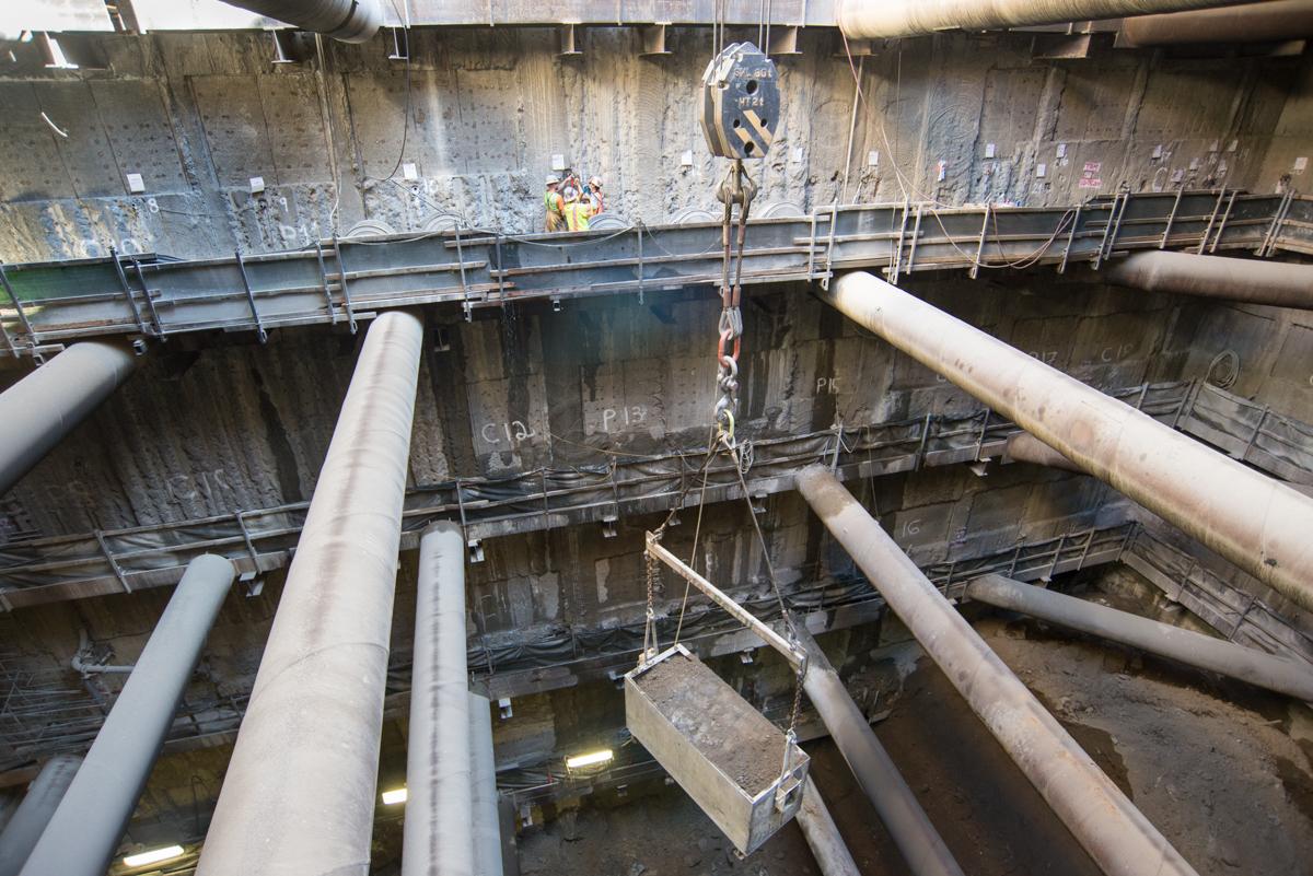 Workers lower bucket of excavated material from underground transit station construction site