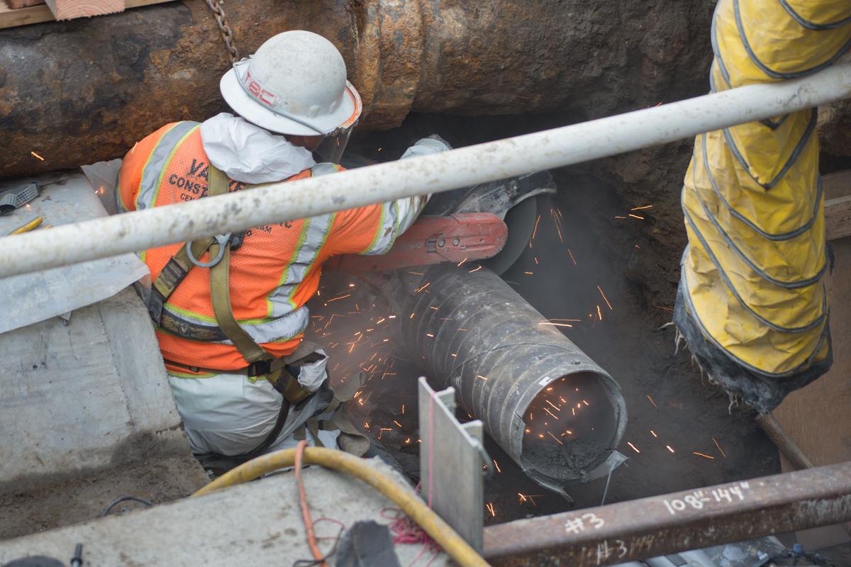 Worker in safety gear cutting water pipe underground at 4th and Brannan Street.