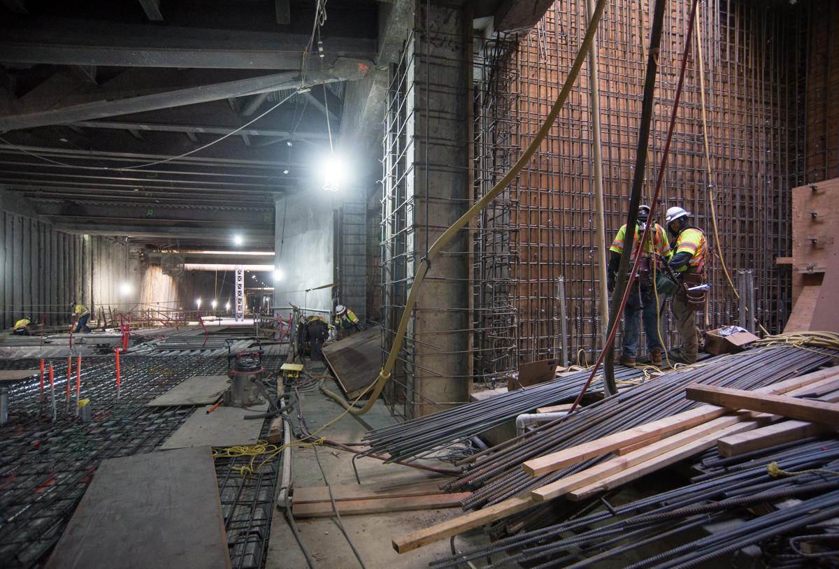 Construction workers install rebar reinforcement in underground transit station concourse at night.