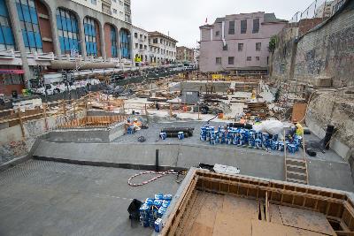 Construction site for Chinatown Station with exposed foundation, equipment, and workers among surrounding buildings.