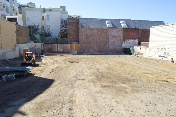Construction site with cleared lot, brick building walls, and yellow equipment at Stockton and Washington streets.