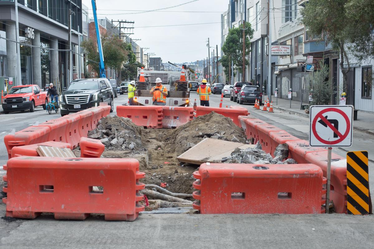 Street construction site with red barriers, excavation, and workers in safety gear on 4th Street.