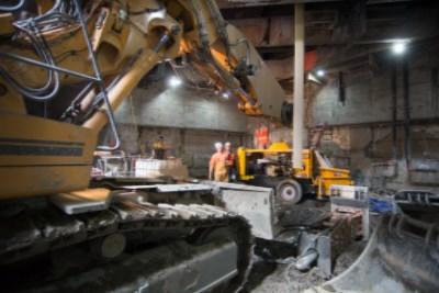 Heavy equipment operates inside an underground construction site, pouring concrete for transit station walls.