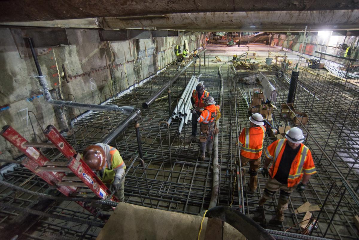 Construction workers in safety gear install reinforcing steel and temporary bracing inside an underground transit station excavation.