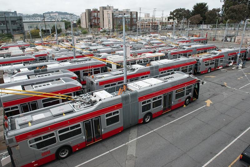 Red and white articulated trolley buses parked in rows at a transit yard facility.