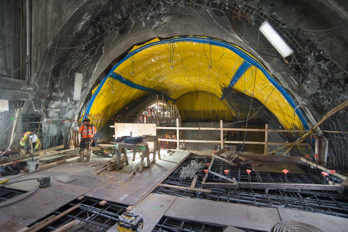 Construction workers install rebar and conduit inside yellow-lined tunnel headhouse at Stockton Street station.