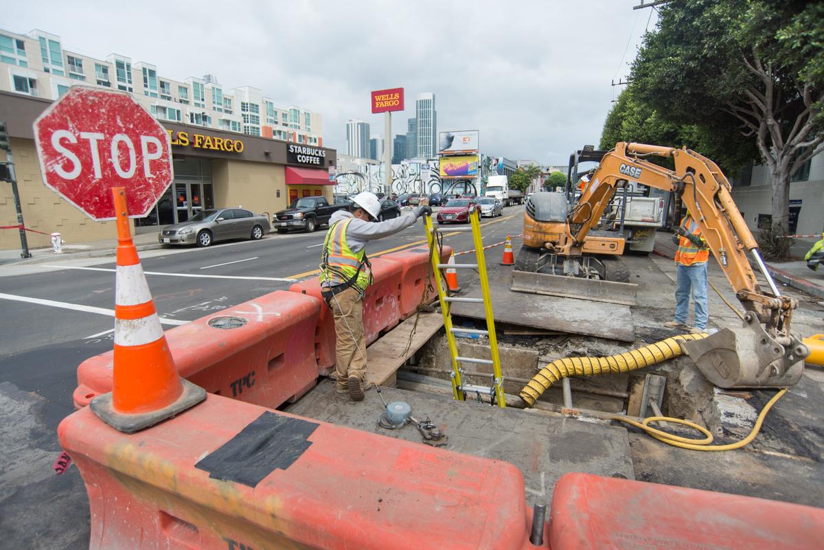 Construction crew performs utility work on 4th Street with excavator and traffic control barriers in place.