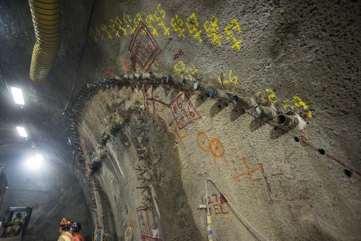 Drill casings mark arched outline of future station cavern in underground tunnel under construction.