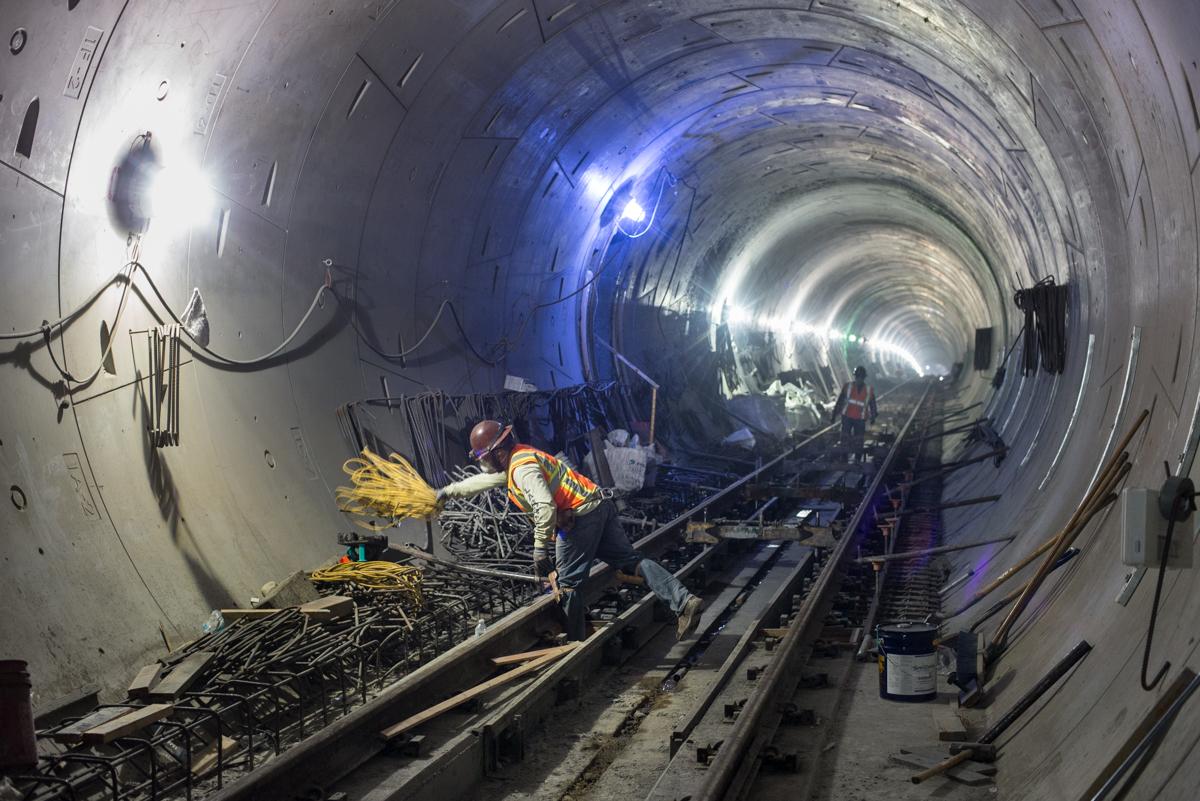 Workers install rails and rebar in a subway tunnel under blue lighting.