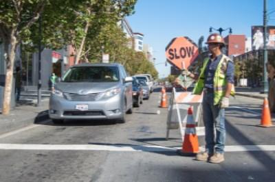 Construction worker holding slow sign directing traffic on city street with barricades and vehicles.