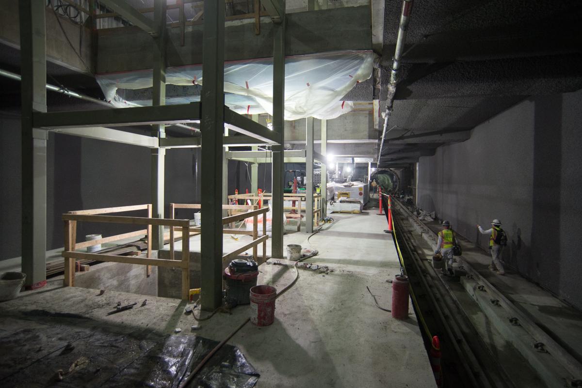 Construction site at transit station with steel framework for elevator shafts, concrete floor, and workers in safety gear.