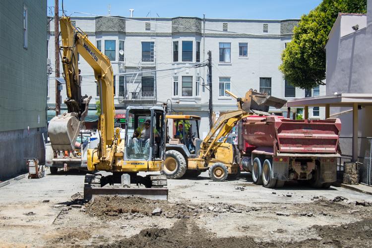 Construction site with yellow excavator loading debris into red dump truck on Washington Street.