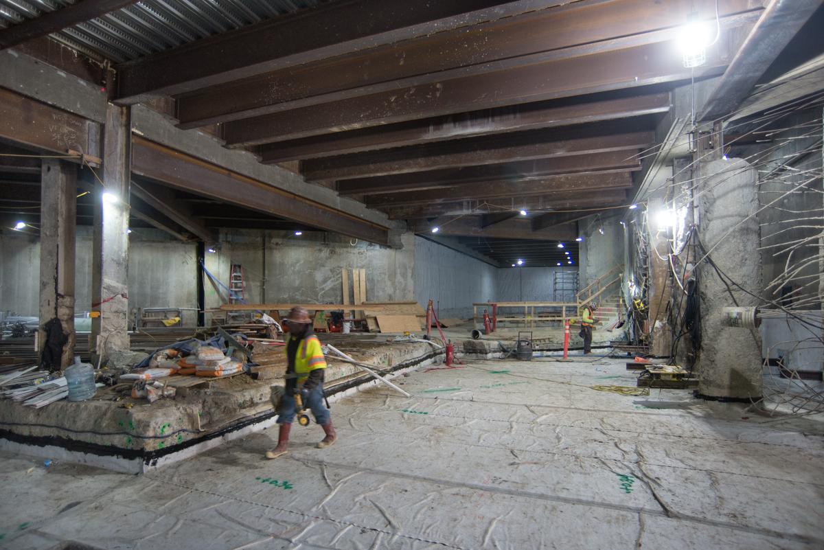 Worker in yellow safety vest operates bulldozer collecting tunnel debris inside underground station construction site.