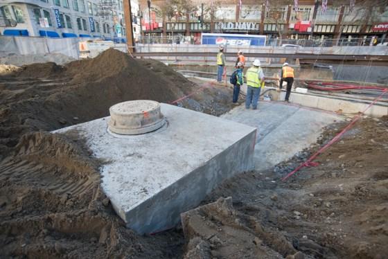 Construction workers perform utility work at 4th and Clementina Street with concrete foundation and excavated soil visible.
