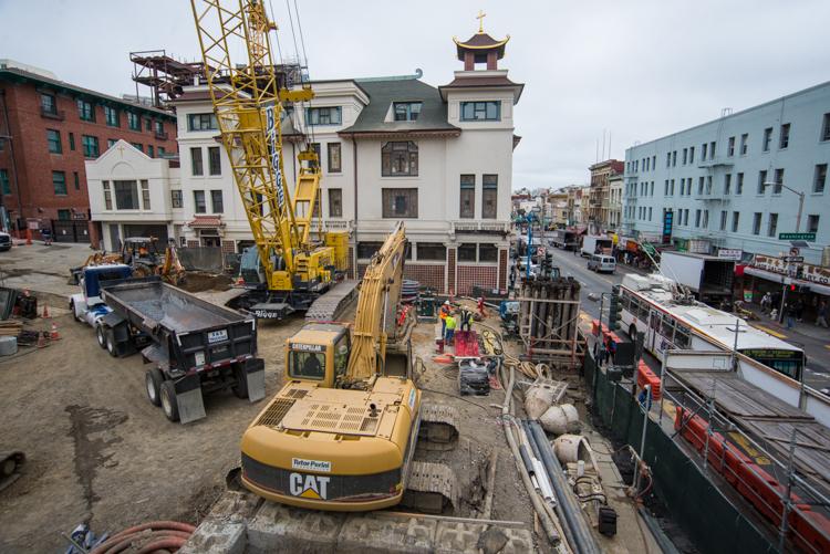 Construction site at Chinatown Station with excavator, dump truck, and workers among surrounding buildings.