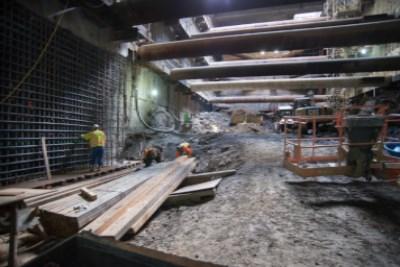 Underground construction site with workers, exposed beams, and excavation equipment in headhouse area.