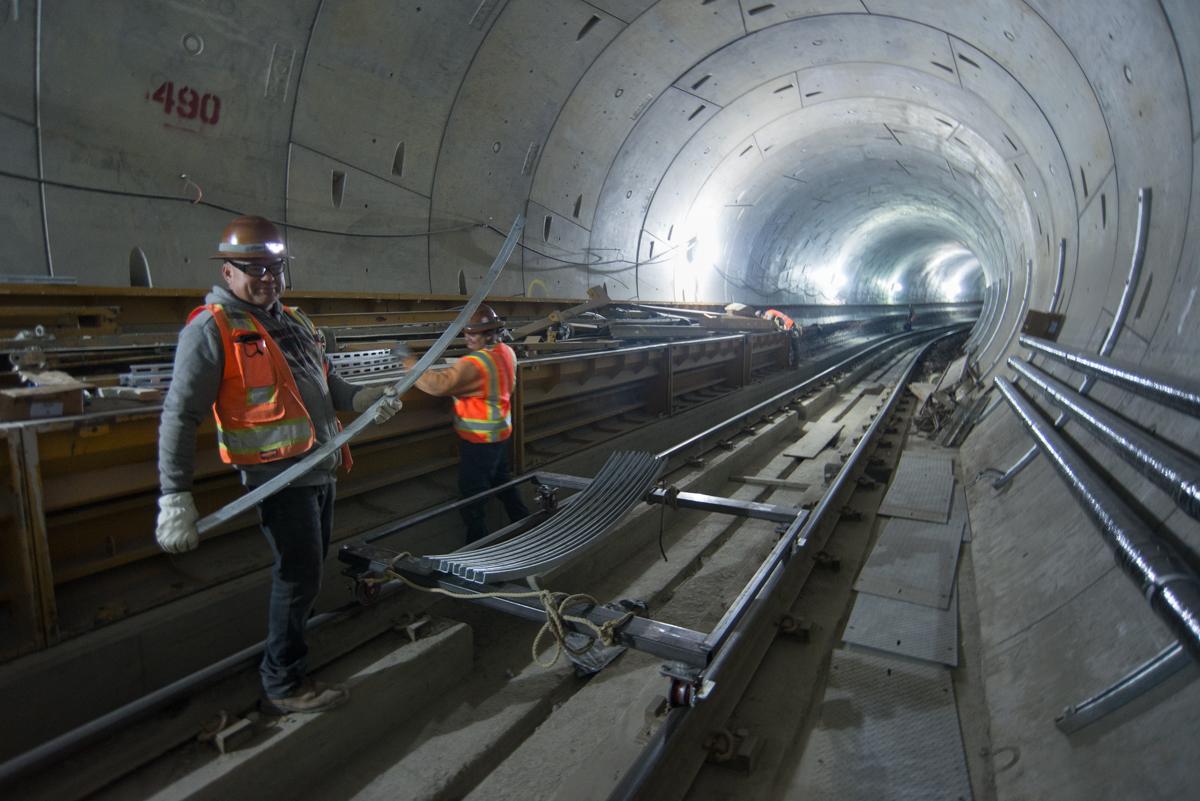 Workers in safety gear unload steel struts from a dolly inside a subway tunnel under construction.