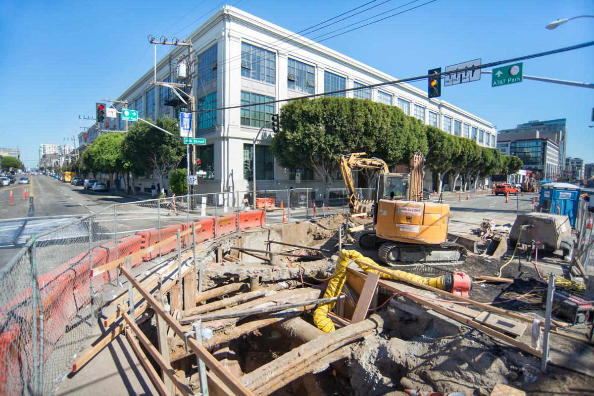 Construction site at 4th and Brannan with excavator and workers preparing sewer line connections for transit project.