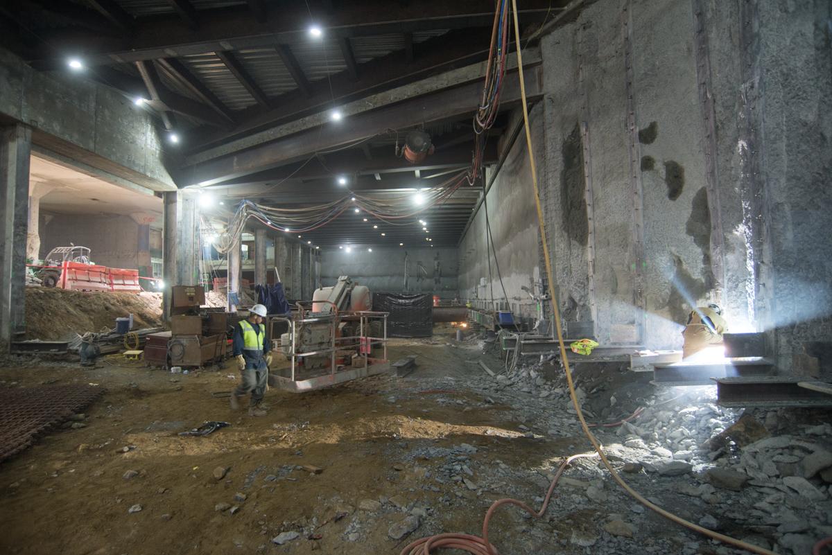 Worker welding steel brackets to concrete walls inside underground transit station construction area.