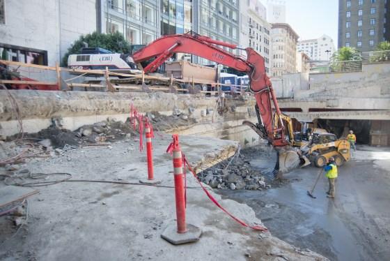 Construction site with red excavator, demolition debris, and workers in safety gear at Union Square Garage.