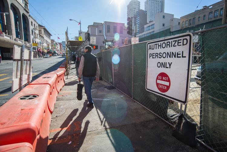 Man walking past fenced construction site with authorized personnel sign on urban street