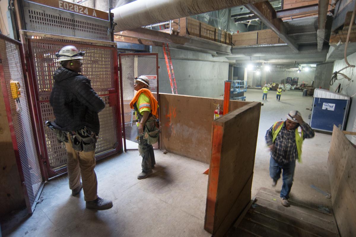 Construction workers in safety gear inside underground transit station during shift change at elevator.