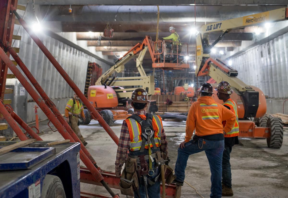 Construction workers in safety gear pause near heavy equipment and concrete forms at an industrial work site.