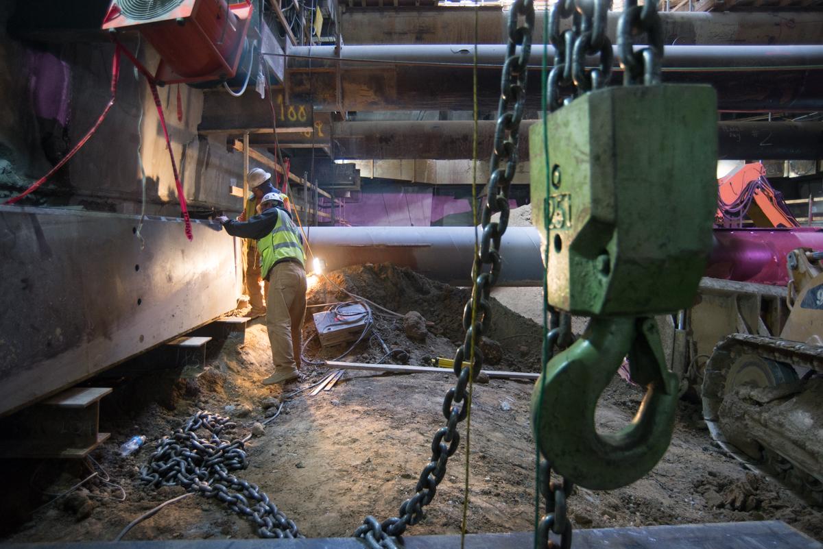 Worker in safety vest welding steel beam inside underground transit station construction site.