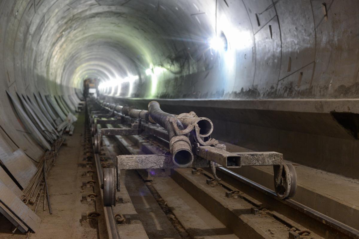 Construction equipment and railway tracks inside an illuminated underground transit tunnel during installation work.