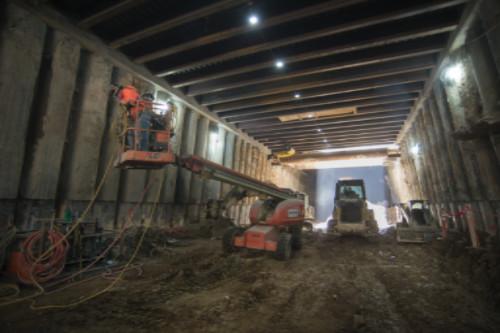 Construction workers welding brackets onto station walls inside an underground transit station box.