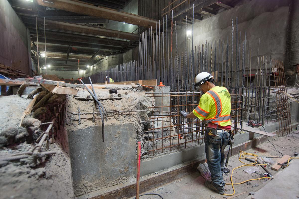 Construction worker in safety gear assembling rebar cage for underground station structural work.