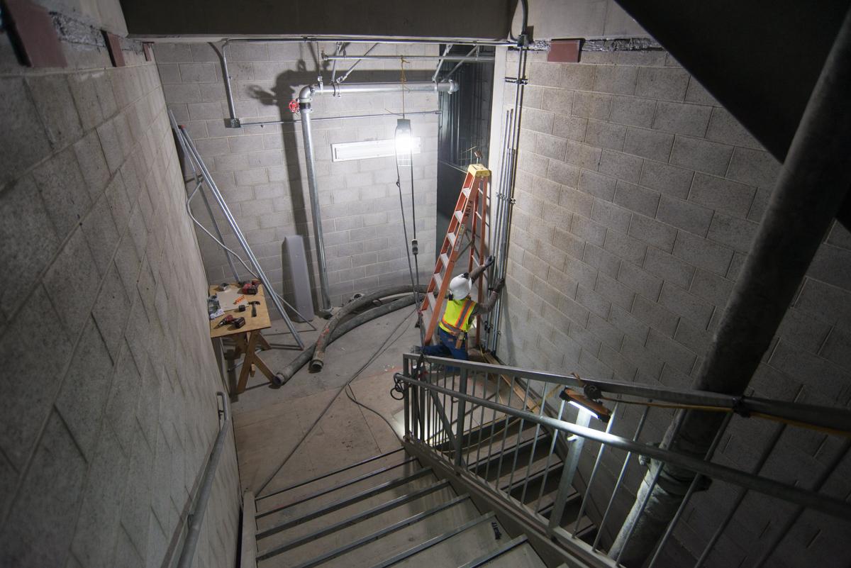 Worker in safety vest installing conduit in underground station box with concrete walls and metal staircase.