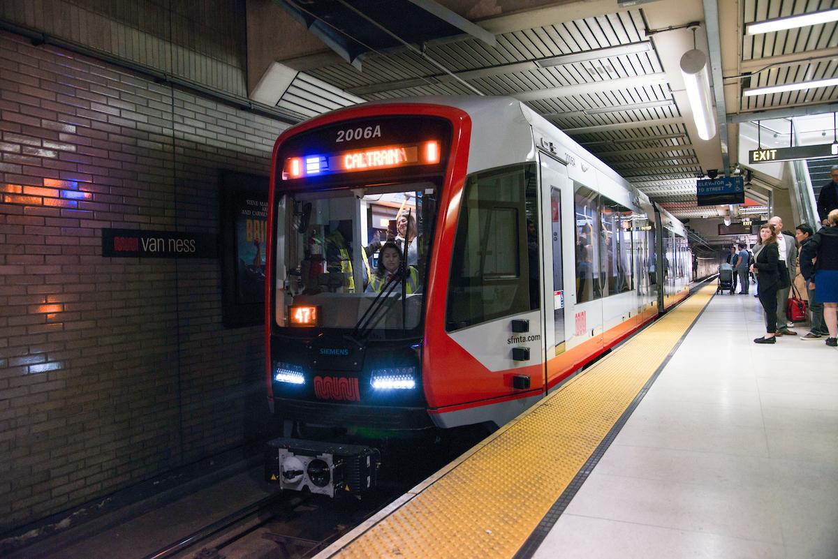 Red and white light rail vehicle 2006A at Van Ness station platform with passengers boarding.