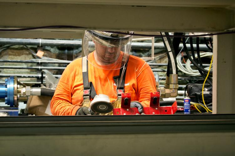 Worker in orange safety gear and clear face shield operating machinery in underground tunnel construction site.