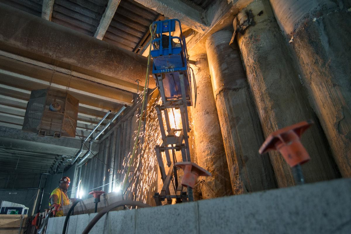 Worker on blue scissor lift performing underground maintenance work beneath city intersection.