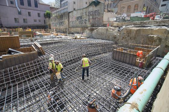 Construction workers in safety vests prepare reinforced steel framework for concrete pouring at Chinatown Station.