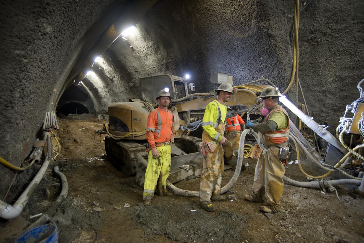 Workers in safety gear operate excavation equipment inside an underground tunnel during construction work.