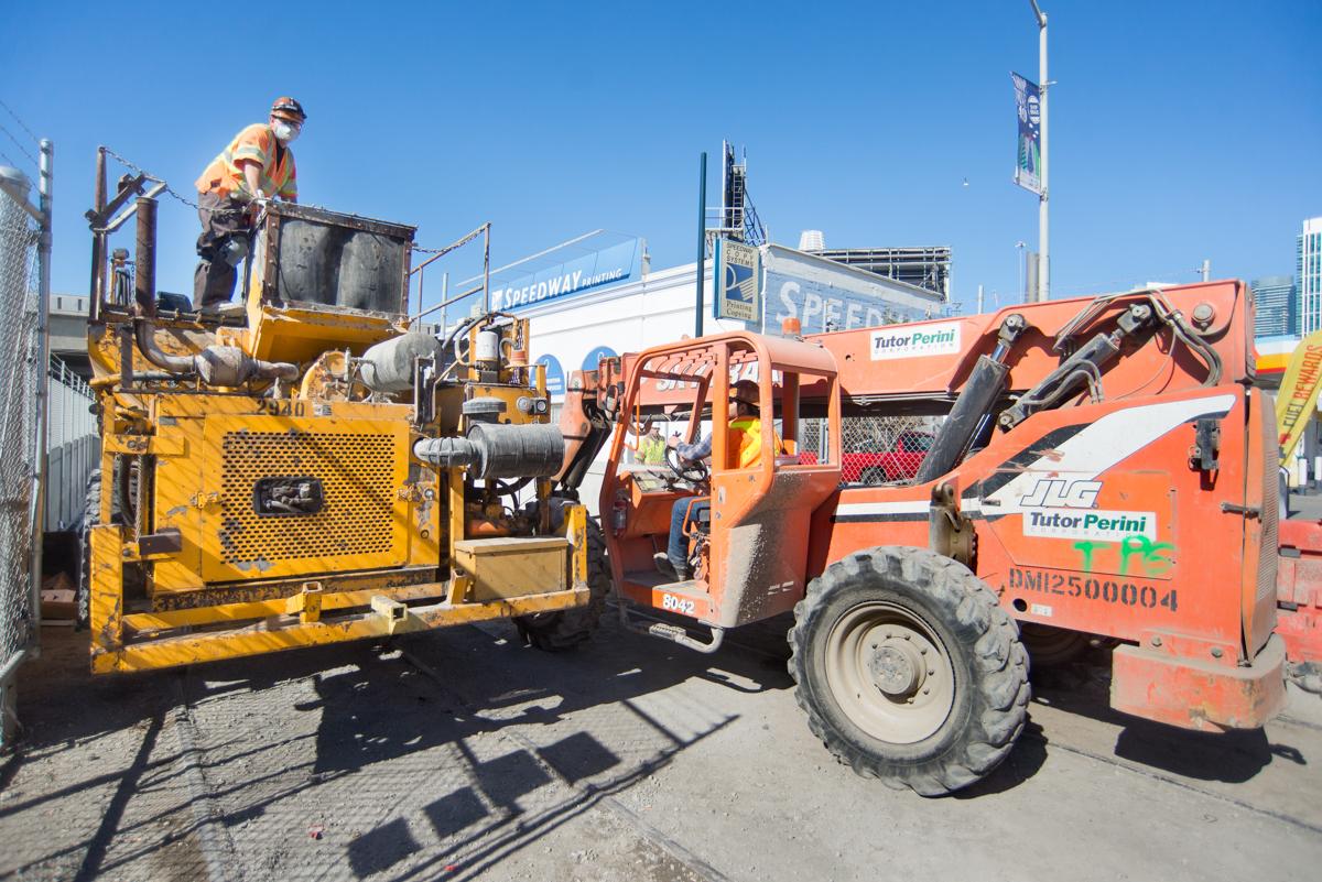 Construction crew operates heavy equipment including a concrete pump truck and telehandler at a transit work site.