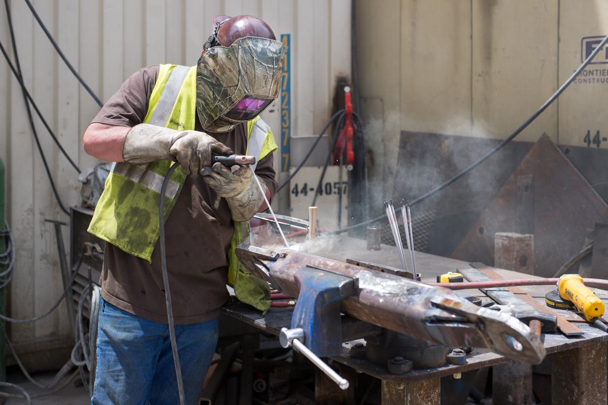 Worker in safety vest and helmet welding metal equipment at construction site.