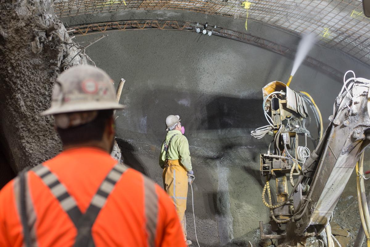 Workers spray shotcrete on cavern walls during underground transit station excavation.