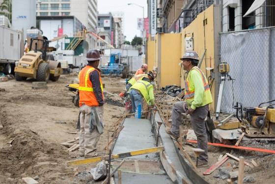 Construction workers in safety vests pour concrete for sidewalk restoration at Stockton and Geary Street.